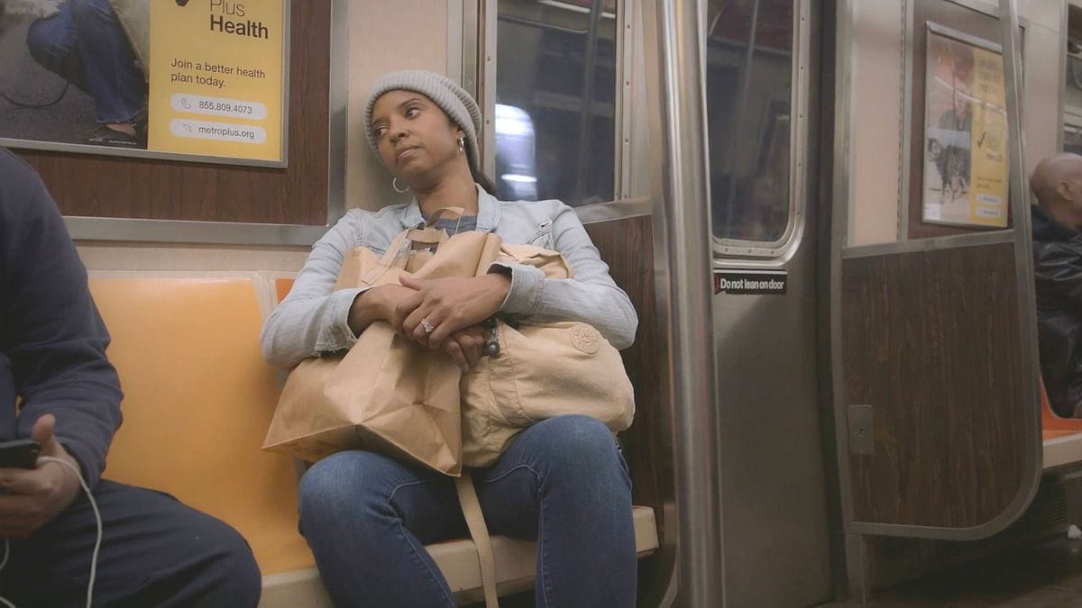 Actor Renee Elise Goldsberry sits on a subway train in a scene from the documentary film Satisfied. (Photo Credit: Courtesy of AURA Entertainment.)